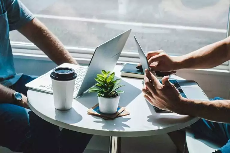 Two professionals working on laptops at a table with coffee and a plant, representing collaborative financial planning and tax services by Jay My CPA