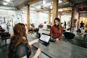 A friendly receptionist assists a customer at a modern salon using a POS system. Small business bookkeeping, sales tracking, and financial management made easy.